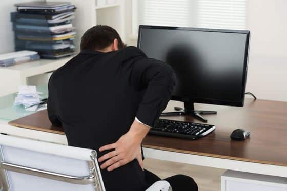 A man hunches over his computer in pain